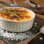 Crab Brulee Recipe: Step-by-Step Guide to Making the Best Crab Brulee 9 A creamy Crab Brûlée in a white ramekin, topped with a caramelized golden sugar crust, garnished with chopped chives, and served on a rustic wooden table.